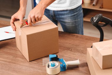 Postane çalışanı, bıçaklı, kapalı gişede paket açıyor, yakın plan.