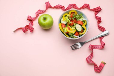Mezura, salata, pembe arka planda elma ve çatal, düz yatak. Metin için boşluk