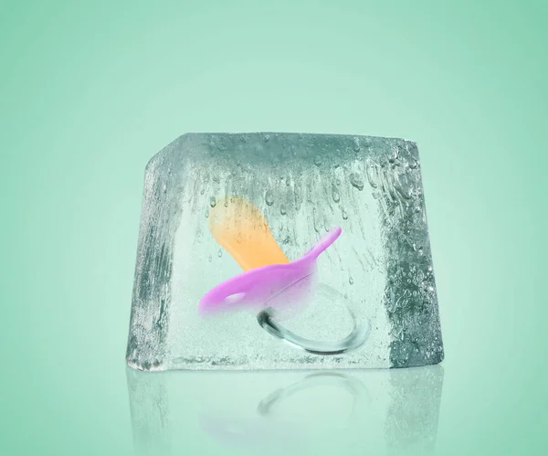 Conservation of genetic material. Baby pacifier in ice cube as cryopreservation on mint color background