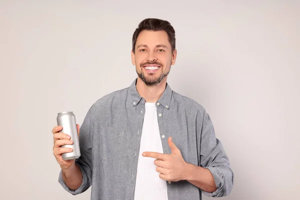 Happy man holding tin can with beverage on light grey background