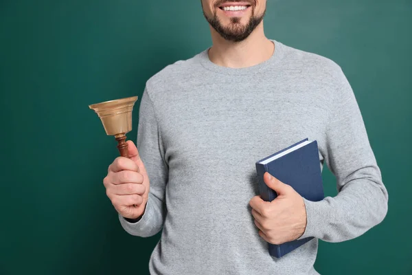 Teacher with school bell near chalkboard, closeup