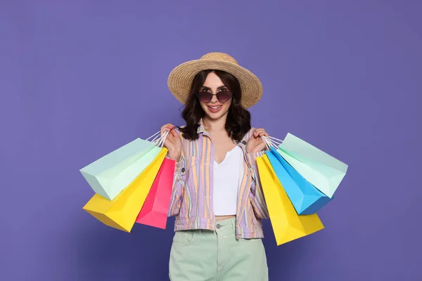 紫の背景に紙のショッピングバッグと美しい若い女性 — ストック写真