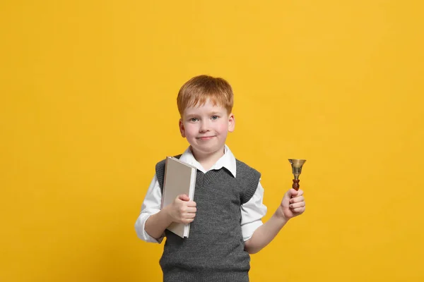 Pupil with school bell and book on orange background