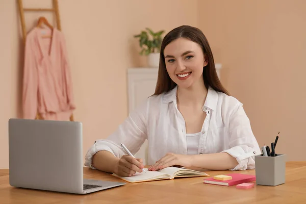 快乐的年轻女子坐在室内木制桌旁的笔记本旁 — 图库照片