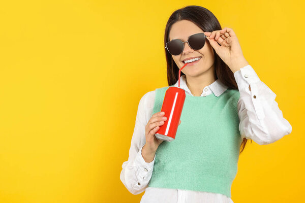 Beautiful happy woman drinking from red beverage can on yellow background. Space for text