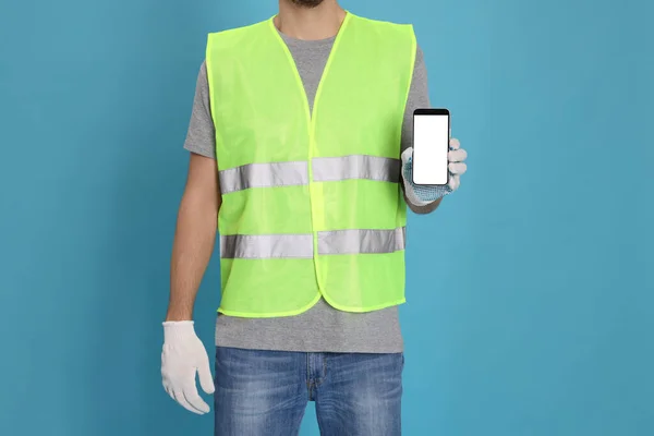 Male industrial engineer in uniform with phone on light blue background, closeup