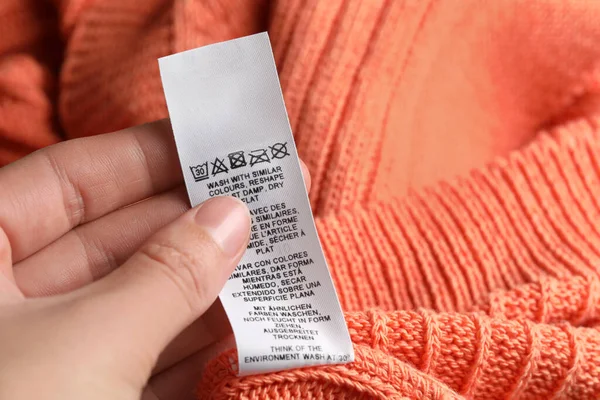Woman holding clothing label on orange garment, closeup