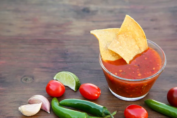 stock image Tasty salsa sauce with tortilla chips and ingredients on wooden table, space for text