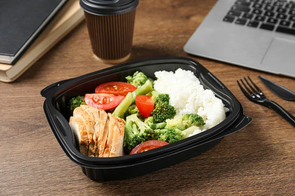 stock image Container with tasty food, laptop, cutlery and cup of coffee on wooden table. Business lunch