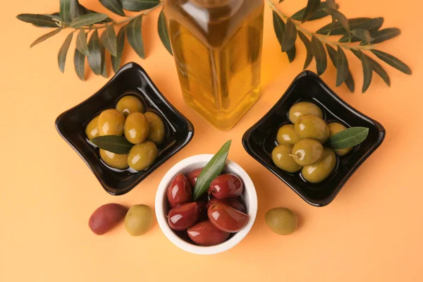Bottle of oil, olives and tree twigs on orange background, flat lay