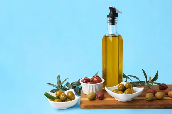 Bottle of oil, olives and tree twigs on light blue background, space for text