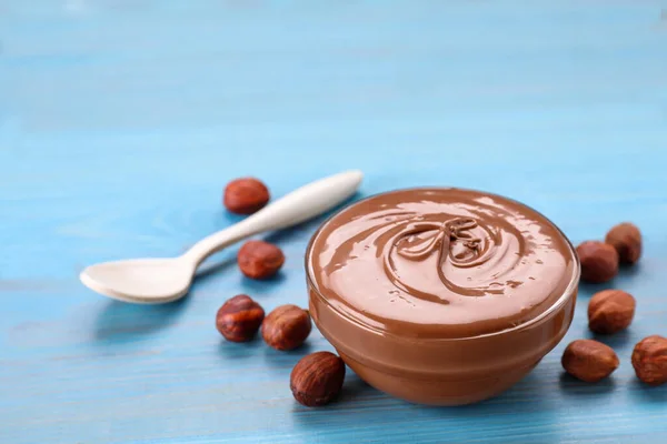 Bowl with tasty chocolate paste and nuts on light blue wooden table