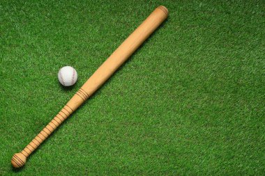Wooden baseball bat and ball on green grass, flat lay. Space for text