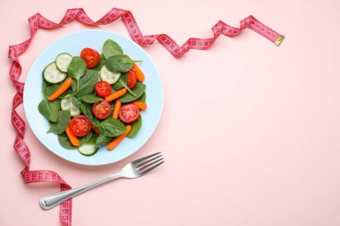 Mezura, çatal ve salata, pembe arka plan, düz yatak. Metin için boşluk