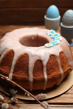 Delicious Easter cake decorated with sprinkles near willow branches and painted eggs on wooden table, closeup