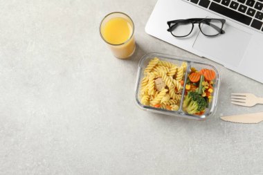 Lezzetli yemek, dizüstü bilgisayar, bardaklar, çatal bıçak takımı ve açık gri masada bir bardak meyve suyu. Mesaj için boş yer var. İş yemeği.