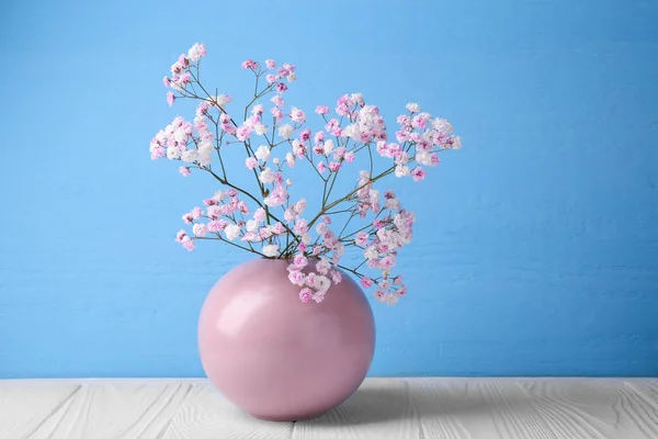 Beautiful dyed gypsophila flowers in pink vase on white wooden table against light blue background