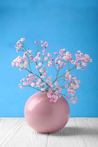 Beautiful dyed gypsophila flowers in pink vase on white wooden table against light blue background
