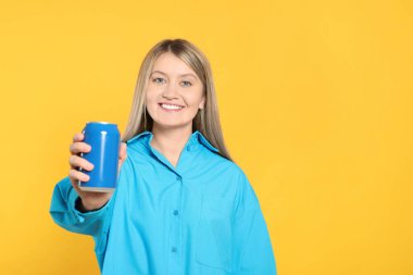 Beautiful happy woman holding beverage can on yellow background. Space for text