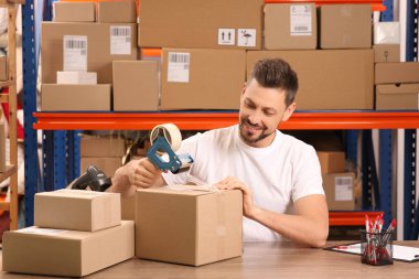 Post office worker packing parcel at counter indoors