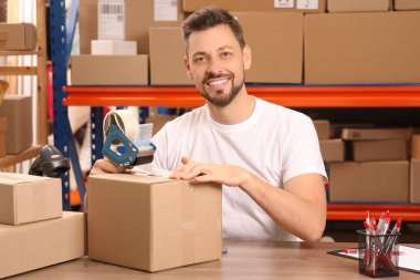 Post office worker packing parcel at counter indoors