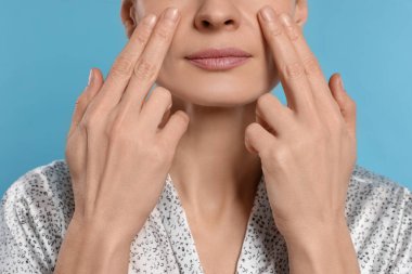 Woman massaging her face on turquoise background, closeup