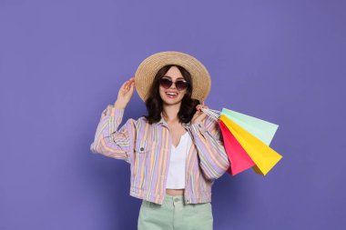 Mor arka planda kağıt alışveriş torbaları olan güzel genç bir kadın.