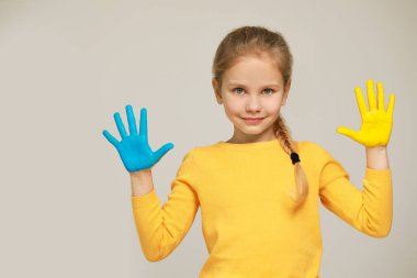 Açık gri arka planda elleri Ukrayna bayrağı rengine boyanmış küçük bir kız, mesaj için yer var. Ukrayna Konseptini Sev