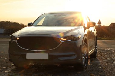 Siyah modern araba gün batımında yola park edilmiş.