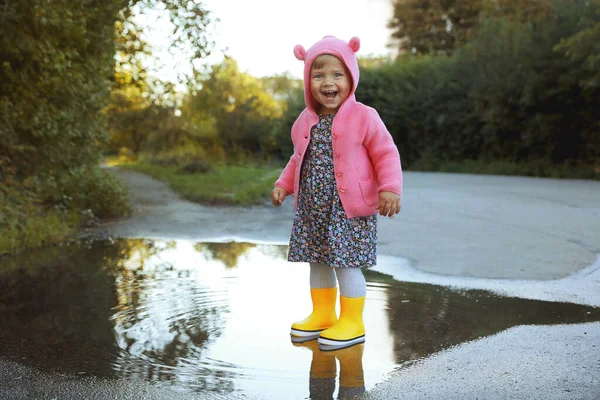屋外の水たまりの中に立ってゴム製のブーツを着ている少女 秋の散歩 — ストック写真