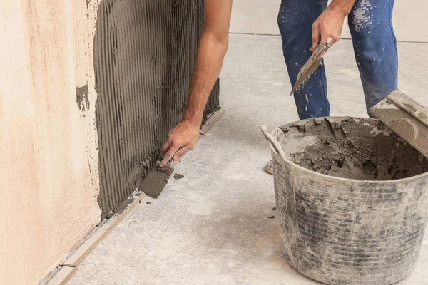 Worker spreading adhesive mix on wall for tile installation indoors, closeup