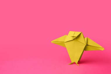 Origami sanatı. Pembe zemin üzerinde el yapımı yeşil kağıt kuş, metin için boşluk