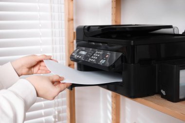 Woman loading paper into printer on shelf indoors, closeup