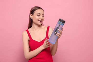 Pembe arka planda şeffaf su şişesi olan genç ve güzel bir kadın.