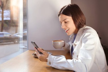 Özel terfi. Kafedeki masada akıllı telefon kullanarak içki içen duygusal genç bir kadın.