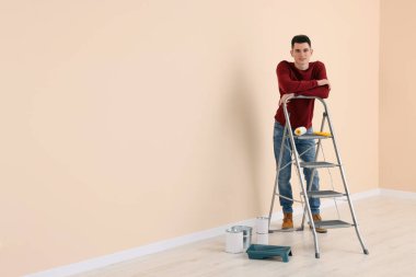 Metal merdiven yanında genç yakışıklı bir adam ve içeride boya aletleri, yazı için yer. Oda yenileme