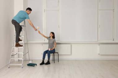 Genç bir kadın, merdivendeki adama içeride paten veriyor. Oda yenileme
