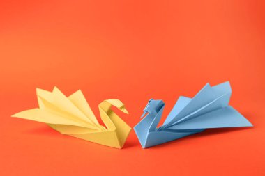 Origami art. Beautiful paper swans on orange background