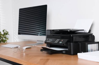 Ofisteki ahşap masadaki bilgisayarın yanında kağıdı olan modern yazıcı