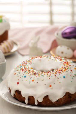 Delicious Easter cake decorated with sprinkles near painted eggs on white wooden table, closeup