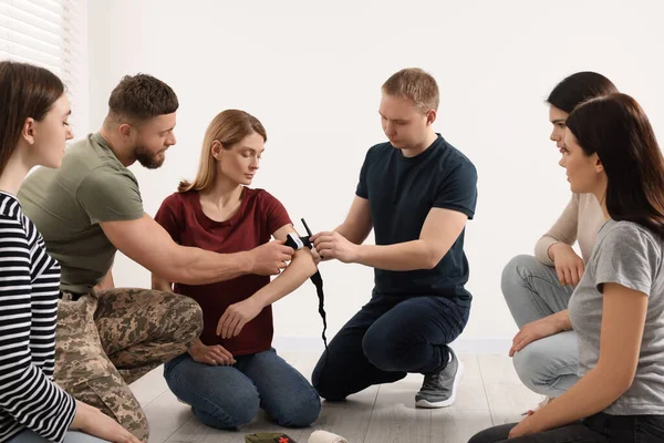 Soldier in military uniform teaching group of people how to apply medical tourniquet indoors
