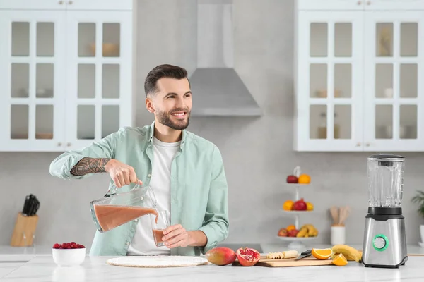 stock image Handsome man pouring tasty smoothie into glass at white marble table in kitchen. Space for text