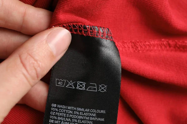Woman holding clothing label on red garment, closeup