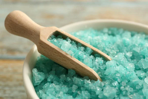 Bowl and scoop with turquoise sea salt on rustic table, closeup