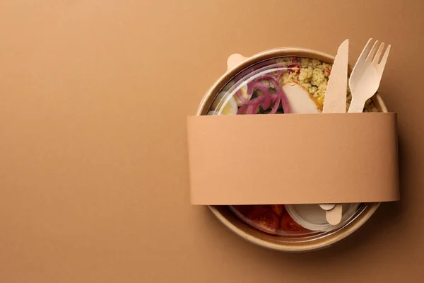 stock image Tasty food in container with wooden fork and knife on beige background, top view. Space for text