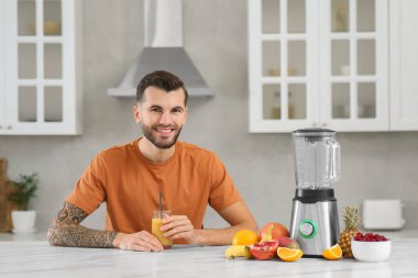 Handsome man with delicious smoothie at white marble table in kitchen