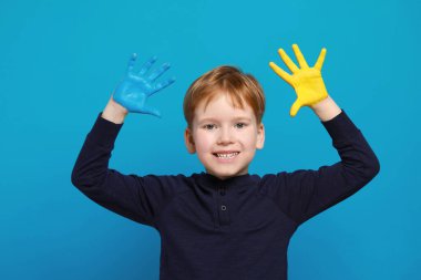 Açık mavi arka planda elleri Ukrayna bayrağı rengine boyanmış küçük bir çocuk. Ukrayna Konseptini Sev