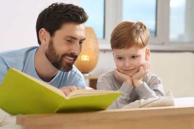 Father reading book with his child on bed at home