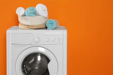 Turuncu arka planda temiz havluları olan çamaşır makinesi, metin için boşluk