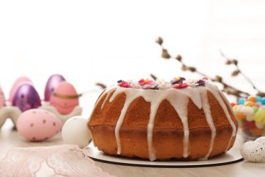 Delicious Easter cake decorated with sprinkles near painted eggs on white wooden table